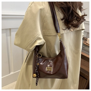 Detail showing brown glossy leather hobo bag with gold letters and woven bell charm