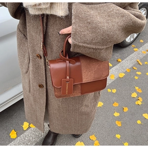 Close-up of retro brown patchwork handbag with leather tag against autumn leaves