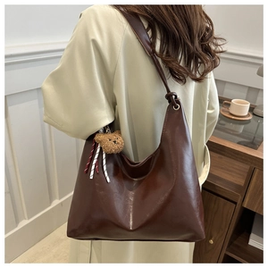 Detail view of deep brown tote bag with bear charm on model wearing beige coat