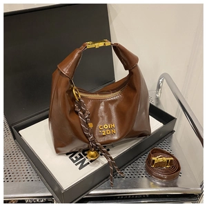 Detail view of dark brown leather half-moon bag with gold logo and woven pendant in a gift box