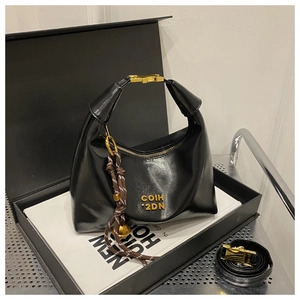 Detail of black glossy handbag with gold logo, metal buckle handle, and woven lanyard