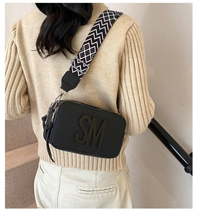 Close-up of black square crossbody bag with embossed SM logo and geometric strap