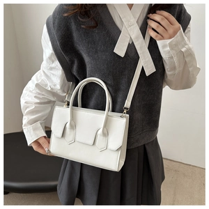 Detail of minimalist white leather handbag with unique cut-out flap and round handle
