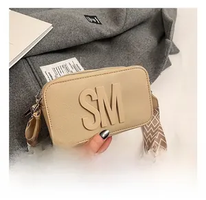 Detail of beige textured leather crossbody bag with SM initials and wave strap