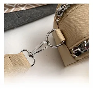 Macro shot of silver swivel hook and cross-grain beige leather detail on a camera bag