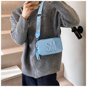Detail of light blue crossbody bag with embossed SM letters and wide patterned strap