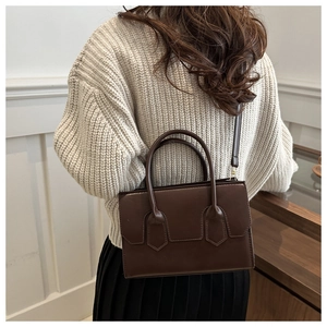 Detail of a dark brown vintage tote bag worn by a model in a minimalist urban setting