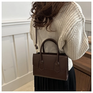 Detail of dark brown structured shoulder bag worn over a beige knit sweater