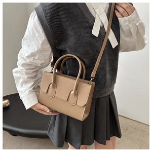 Detail view of a beige minimalist crossbody bag with top handles and adjustable strap
