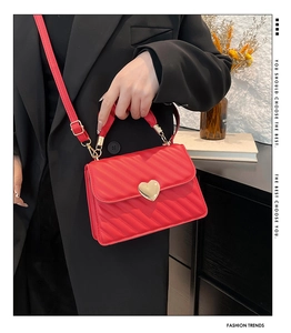 Detail of red quilted crossbody bag with gold heart lock shown on black blazer