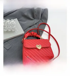 Dettaglio borsa rossa in PU con chiusura a cuore dorata e manico a pieghe su abito