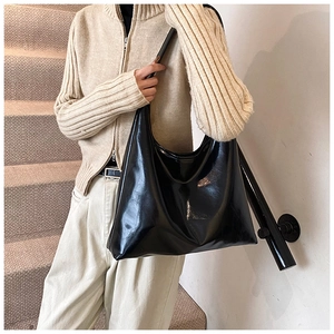 Detail of a black glossy patent leather tote bag styled with a beige knit sweater