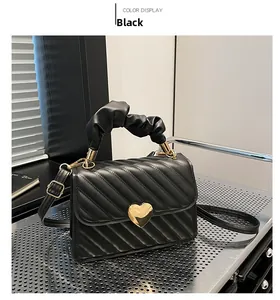 Close-up of black quilted bag featuring gold heart metal buckle and pleated handle detail