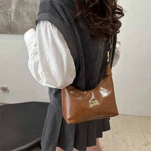 Retro brown glossy leather crescent bag with gold logo shown on model over grey vest
