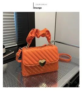 Detail of orange ruched handle handbag with golden heart turn-lock and quilted texture