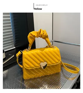 Detail of yellow pleated handbag with heart-shaped gold clasp and adjustable shoulder strap