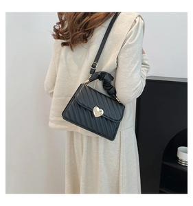 Detalle de bolso negro acolchado en V con cierre de corazón dorado y asa fruncida de moda