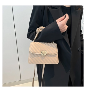Dettaglio borsa beige testurizzata con chiusura a cuore d'oro e manico a pieghe