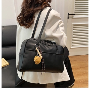 Detail of a black oversized shoulder tote with baseball charms worn over a white blazer