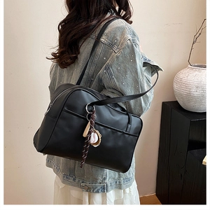 Side view of black matte leather shoulder bag with baseball charm on a model
