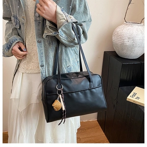 Detail of black leather tote bag with unique baseball glove and bat charm hanging from handle