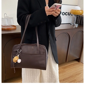 Detail of coffee brown tote bag with baseball charm on a model in black blazer