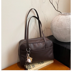 Detailed macro view of matte chocolate brown leather pillow bag with baseball keychain