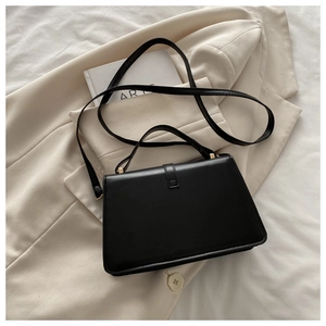 Detail of a minimalist black structured handbag with gold hardware and top handle strap