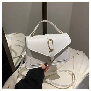 Close-up of white PU leather handbag with gold buckle held by hand in a cozy setting