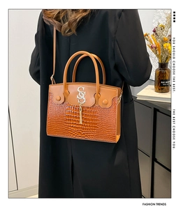 Détail du sac marron motif crocodile avec logo SS entrelacé et pompon doré élégant