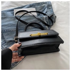 Detail of black faux leather crossbody bag featuring a striking gold bar-shaped metal lock