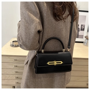 Close-up of elegant black handbag with gold metal lock on brown herringbone blazer