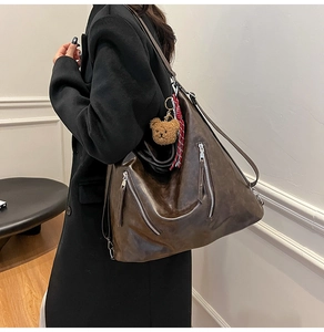 Detail of dark brown tote bag with decorative side zippers and brown plush bear charm