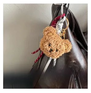 Close-up of a teddy bear plush keychain with a woven rope on a brown leather bag