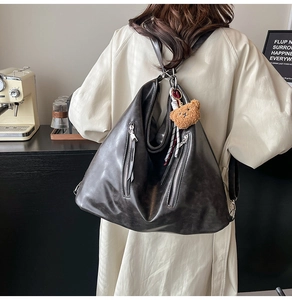 Détail du sac à dos vintage en cuir noir avec fermetures éclair et un charmant pendentif ours