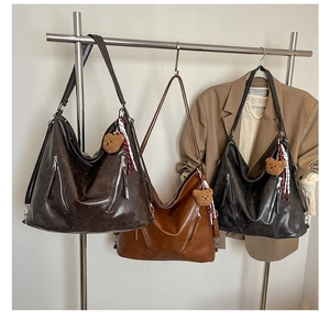 Three leather hobo bags in brown and black with bear charms and scarves on a rack