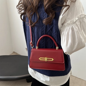 Red structured crossbody bag with gold lock and top handle shown on a model
