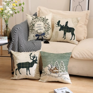 Set of four Christmas linen pillow covers with winter wreath and reindeer on a sofa