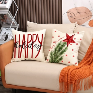 Set of two Christmas linen pillow covers with festive lettering on a cozy sofa