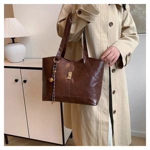 Détail du cabas en cuir marron foncé avec boucle en métal doré et pendentif tressé chic
