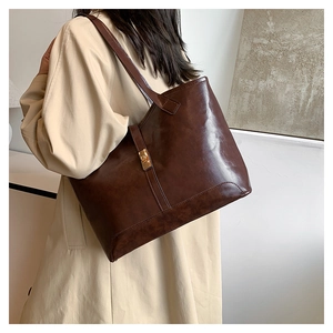 Détail du grand cabas en cuir marron avec boucle dorée porté sur un trench-coat beige