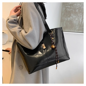 Detail of glossy black tote bag with gold swivel lock and unique bell pendant charm