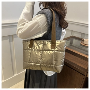 Fashionable gold quilted tote bag with brown fabric strap worn by a model in interior