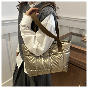 Close-up of golden quilted puffer tote bag with wide brown strap shown on a model