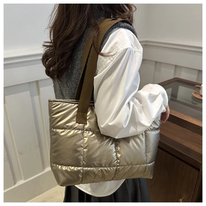 Side view of a champagne metallic quilted tote bag worn by a model in a cozy indoor setting