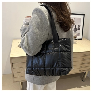 Detail of black quilted puffer tote bag in glossy nylon on model shoulder in office