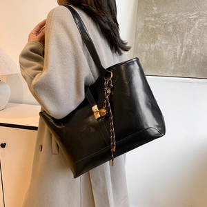 Sac cabas chic en cuir noir brillant avec fermoir doré et pendentif, porté à l'épaule