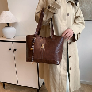 Sac cabas vintage marron foncé avec boucle dorée et pendentif dans un décor minimaliste