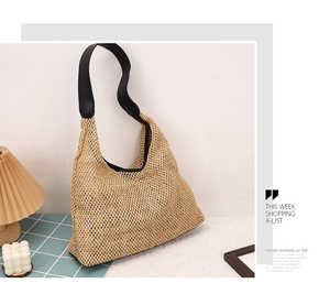 Detail of hollow woven straw tote bag with black leather shoulder straps on a table