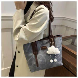 Detail of grey textured tote bag with leather handles and white cloud plush charm